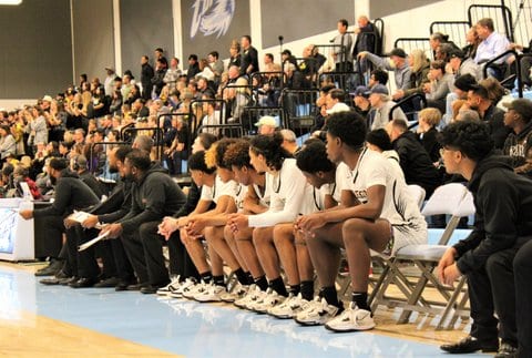 Boys high school basketball players sitting on folding chairs on the sidelines with fans behind them