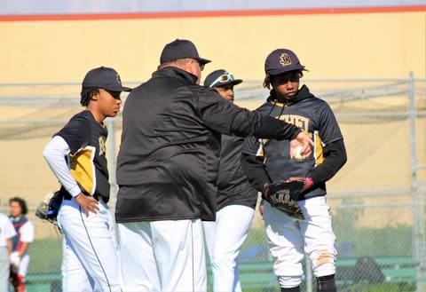 A heavier-set white male baseball coach standing with three Black teen boys in uniform