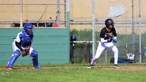 A high school baseball player squares around to bunt with the catcher in a standing crouch behind him.