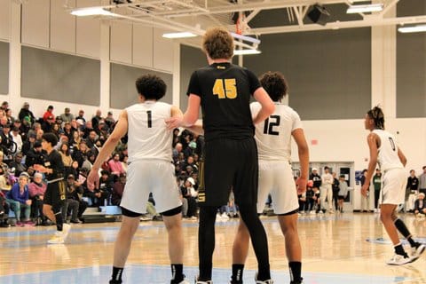 A 7-foot-tall white basketball player standing between two opponents who are significantly shorter than him.