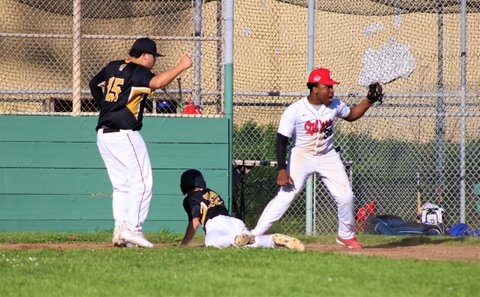 Players in opposing uniforms both react positively to getting another player out on the basepaths in a high school baseball scrimmage.