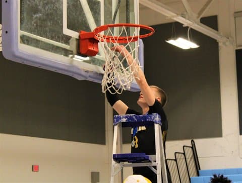 A white basketball player stands on a ladder as he cuts the net