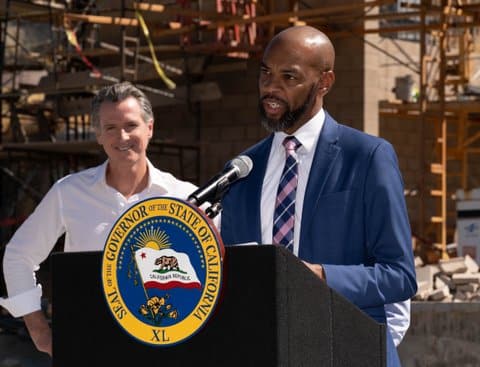 Antioch Mayor Lamar Thorpe, a Black man, stands at a lectern with the Seal of the Governor of the State of California. Looking on with a smile is Gov. Gavin Newsom.