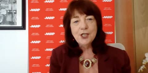 A white woman in front of a red backdrop that features the AARP logo repeatedly