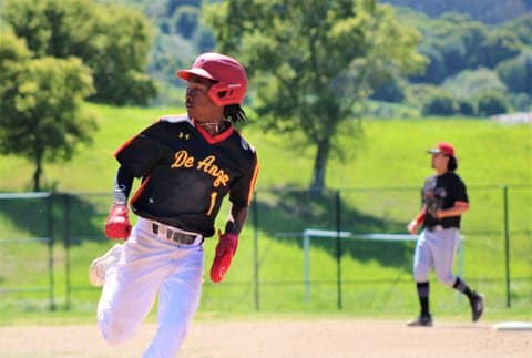 A Black high school baseball player looking toward the outfield while running the bases