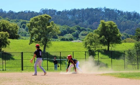 A high school baseball game being played in front of a green, hilly area with trees