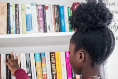 A young Black girl photographed from behind looking at a bookshelf