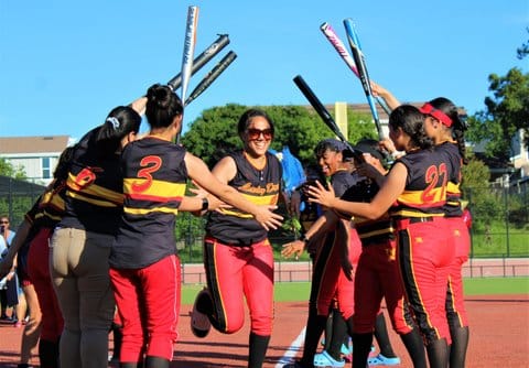 A high school softball player running between two rows of teammates, some holding bats aloft