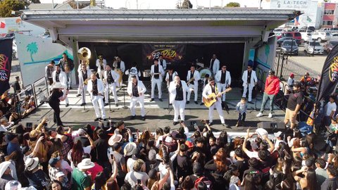 Overhead shot of a crowd watching several Hispanic men in white suits onstage for a musical performance.