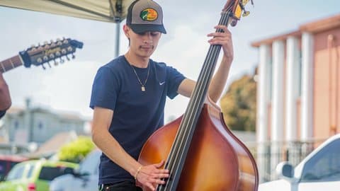 A young Hispanic man wearing a Bass Pro Shops ballcap plays an upright double bass
