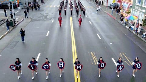 A row of young women, who are each carrying a letter to spell out Richmond, lead a high school marching band down a city street