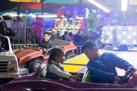 Kids driving different styles of little cars at a carnival.
