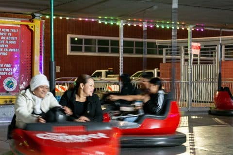 Two women in one red bumper car and two boys in another. The boys and cars are somewhat blurry because they're in motion.