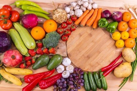 Assorted colorful fruits and vegetables including strawberries, chiles, tomatoes, mushrooms, carrots, grapes, avocado, garlic, red onion, citrus, bananas and broccoli