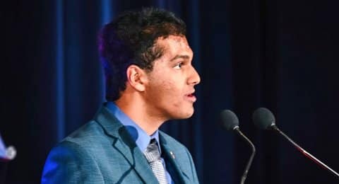An Indian American young man in a suit at a microphone