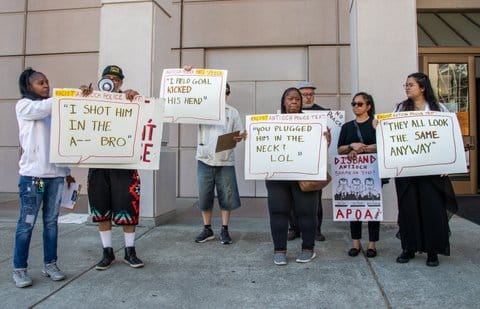 People holding signs with the following messages "I shot him in the a-- bro,"I field goal kicked his head,"you plugged him in the neck? LOL" and "they all look the same anyway." Three also say "racist antioch police text" and one says "antioch police hate speech." Another sign reads "disband antioch APOA now!" "shame on you police officers association" with three drawings of a man covering first his eyes, then his ears, then his mouth.