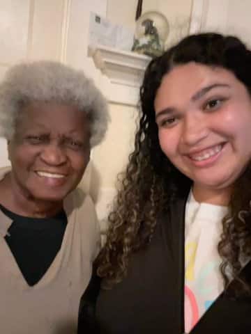 An older Black woman with short gray hair and a biracial teen girl with long curly hair, both smiling.