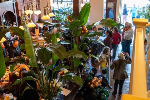 Interior shot of a restaurant looking down on several plants and people standing around or sitting at tables