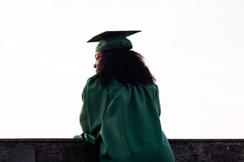 View from behind of a Black person with long, curly hair wearing a green graduation cap and gown