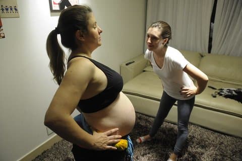 A pregnant woman in a black bra and her doula, also a woman