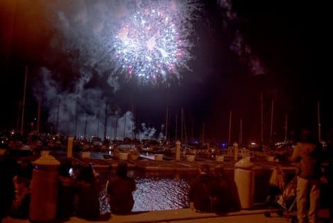 People sitting or standing on docks watching fireworks