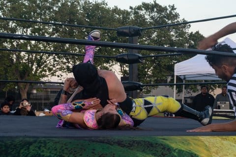 Two wrestlers, one a woman and the other a man, compete in an outdoor ring.