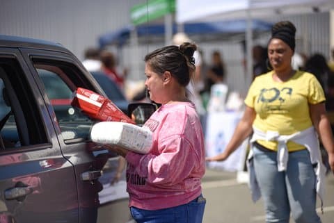 A woman holding two packs of diapers and handing one through a car window
