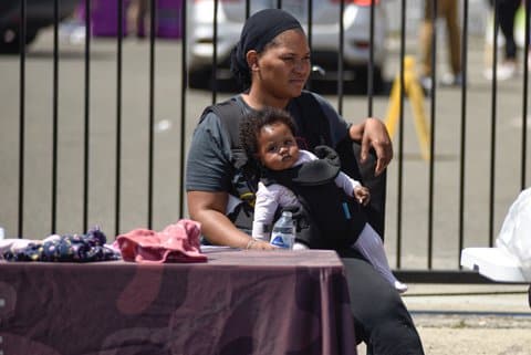 A Black woman sitting outside with her baby strapped to her. The baby is looking toward the camera.