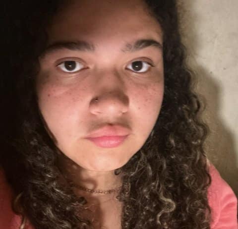 Close up of teenage girl who is mixed Black and white. She has long, curly hair and a serious expression on her face