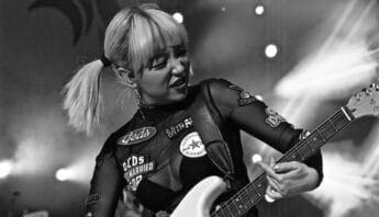 Black and white photo of a woman with short blond hair in pigtails playing electric guitar