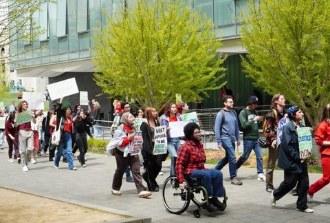 A group of young people protesting. Many are walking and carrying signs. One is in a wheelchair