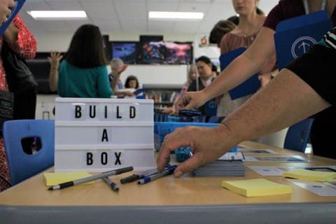 Person's hand reaching for a pen next to a sign that reads build a box