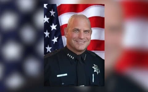 Pinole police chief Neil Gang, a white man in uniform, in front of a U.S. flag backdrop