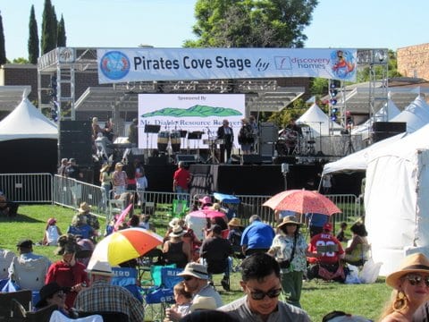 People sitting on grass in front of Pirates Cove Stage
