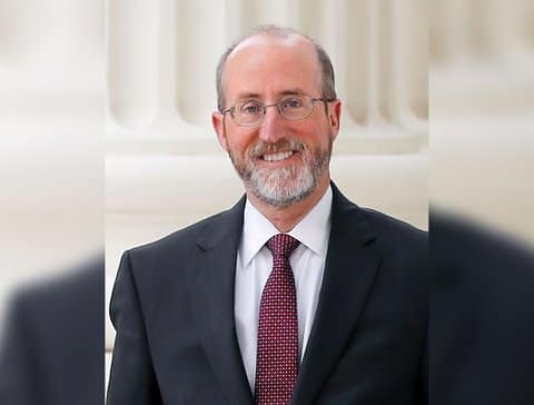 A smiling, balding white man with graying beard, glasses, suit and tie