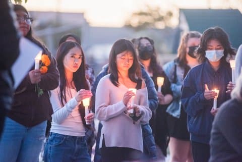 People standing together, holding candles. The picture is focused on two young Asian women