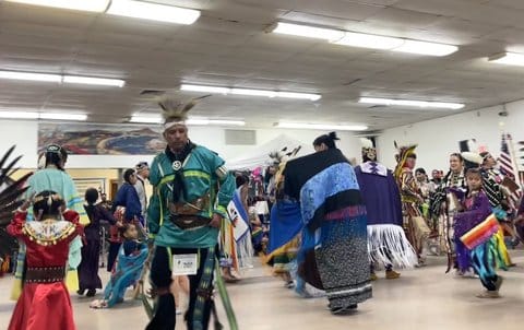 Native American adults and children dancing in traditional regalia