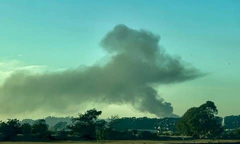 A large plume of smoke against a hazy sky, which looks partly blue but also a bit yellow, brown and green.